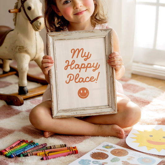 Child holding a framed picture with 'My Happy Place!' text in a room with toys and art supplies.